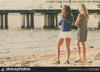 Relaxation and leisure. Attractive mid aged women talking resting on beach. Female tourists relax near to water place on nature.. Two women talking resting on beach.