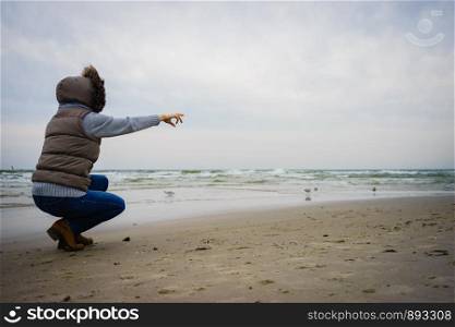 Relaxation and leisure. Woman walking on beach. Female tourist pointing with finger near to water place on nature. Autumn cold season.. Woman walking on beach, autumn cold day