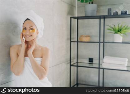 Relaxation at spa resort. Happy girl wrapped with her hair and body in towels applies eye patches. Young hispanic lady takes shower at home. Face skin rejuvenation and collagen nourishing.. Relaxation at spa resort. Happy girl wrapped with her hair and body in towels applies eye patches.