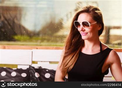 Relaxation concept. Young woman wearing black dress bright jacket sitting on bench. Fashionable female model resting spending free time.. Young woman relax on bench.