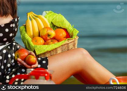 Relaxation during summertime concept. Woman holding picnic basket with fruits. Water sea in background.. Woman holding picnic basket with fruits