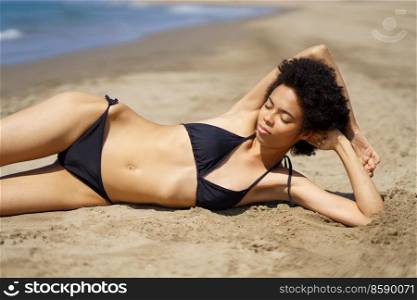 Relaxed African American female lying on the sand of a tropical beach sunbathing. Black girl tanning.. Relaxed African American female lying tanning on the sand of a tropical beach sunbathing.