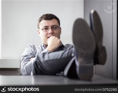 Relaxed casual young business man with legs on desk in office. Shallow depth of field.