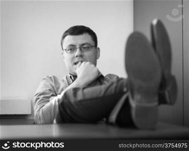 Relaxed casual young business man with legs on desk in office. Shallow depth of field.