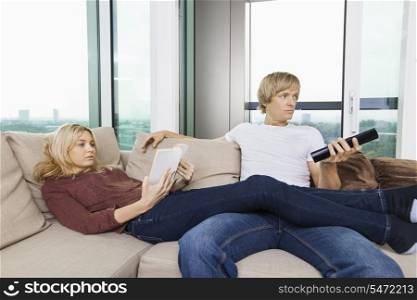 Relaxed couple reading book and watching TV in living room at home