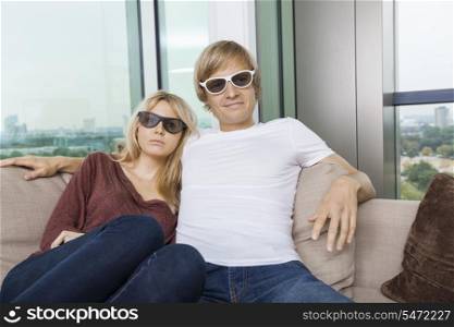 Relaxed couple wearing 3D glasses while sitting on sofa at home