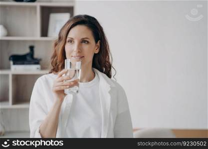 Relaxed european woman is drinking transparent pure water at home. Happy girl is holding glass and smiling. Filtered water for healthy lifestyle. Morning routine for beauty and wellness.. Relaxed european woman is drinking pure water at home. Happy girl is holding glass and smiling.
