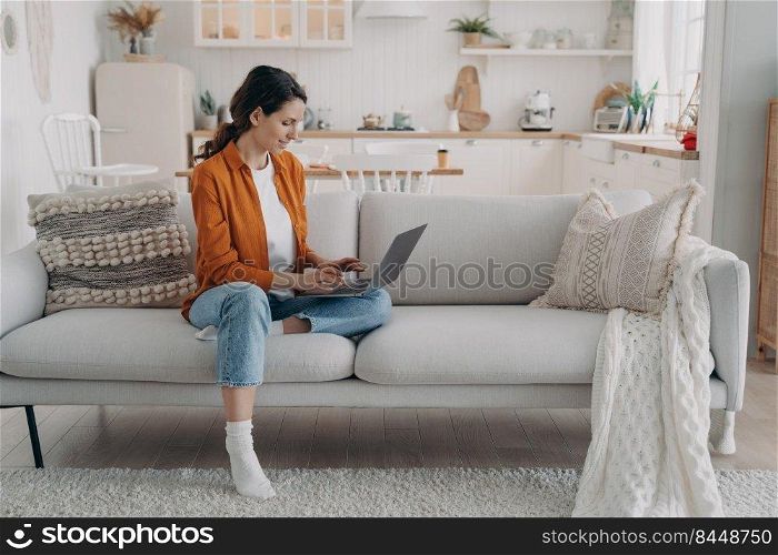 Relaxed european woman working with computer at home. Caucasian Lady is sitting on couch. Manager is consulting from home. Remote work in cosy living room, kitchen interior.. Relaxed european woman working with computer at home. Manager is consulting. Remote work.
