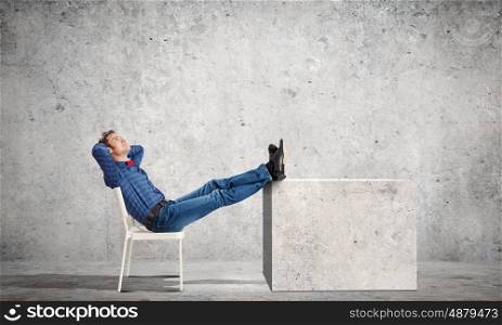 Relaxed guy. Young man sitting in chair with legs up and relaxing