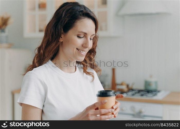 Relaxed happy woman with cup of coffee at home. Daily routine. Young attractive housewife alone at kitchen in morning. Scandinavian stylish interior. White modern furniture.. Young attractive housewife with cup of coffee at kitchen in morning. Scandinavian stylish interior.