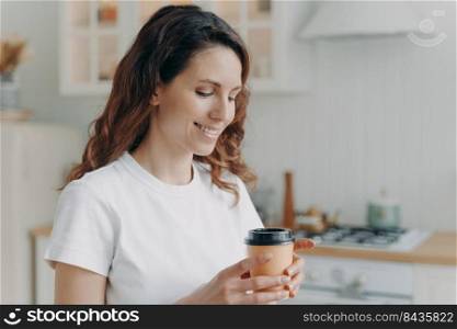 Relaxed happy woman with cup of coffee at home. Daily routine. Young attractive housewife alone at kitchen in morning. Scandinavian stylish interior. White modern furniture.. Young attractive housewife with cup of coffee at kitchen in morning. Scandinavian stylish interior.