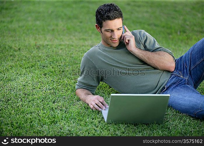 Relaxed man using phone and computer laid on the grass