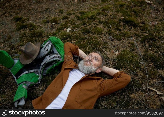 Relaxed mature man hiker rest lying on grass in forest enjoying beautiful view on sky listening to birds songs. Relaxed mature man hiker rest lying on grass in forest