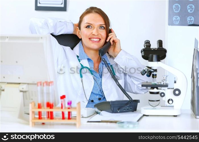 Relaxed medical doctor woman sitting at office table and talking on phone&#xA;