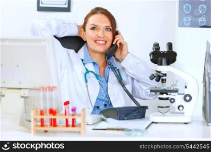 Relaxed medical doctor woman sitting at office table and talking on phone&#xA;