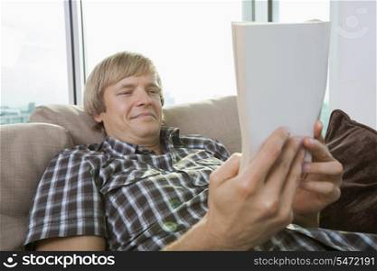 Relaxed mid-adult man reading book in living room at home