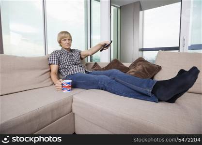 Relaxed mid-adult man watching television while having coffee on sofa at home