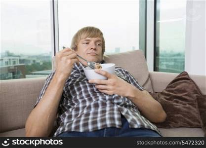 Relaxed mid-adult man with bowl of cereal in living room at home