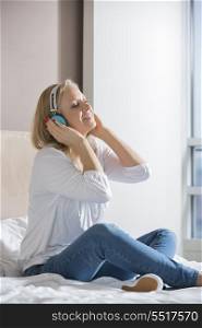 Relaxed mid adult woman enjoying music on headphones in bedroom