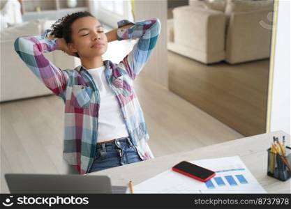 Relaxed mixed race girl student rests, enjoying pause while learning at laptop, sitting at desk. Young teen lady relaxing on workplace with closed eyes after doing homework, putting hands behind head.. Mixed race girl student resting, enjoying pause while learning at laptop, sitting at desk at home