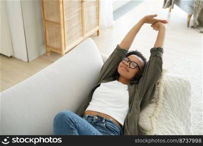Relaxed mixed race young girl stretching while lying on comfortable sofa. Pretty teen lady waking up after day sleep, afternoon nap, resting on couch with pillow, feeling lazy on weekend.. Relaxed mixed race young girl stretching after day sleep, afternoon nap, lying on comfortable sofa