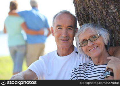 Relaxed older couple sitting in the shade of a tree on a summer&rsquo;s day