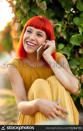 Relaxed red haired woman with a mobile in the park in a sunny day