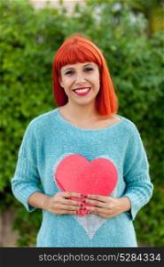 Relaxed red haired woman with blue jersey in the park holding a red heart