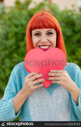 Relaxed red haired woman with blue jersey in the park holding a red heart