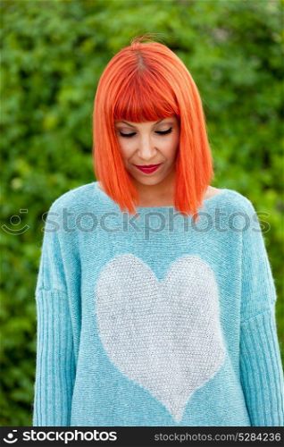 Relaxed red haired woman with blue jersey in the park looking at down