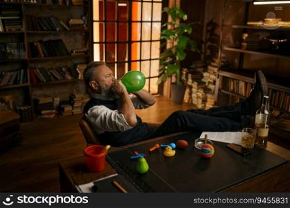 Relaxed senior businessman wearing elegant clothes blowing up balloon while sitting at home office. Relaxed senior businessman blowing up balloon while sitting at home office