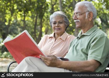 Relaxed senior man reading book with woman at park