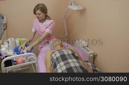 Relaxed senior woman lying on the table with eyes closed getting face cleaning by professional beautician. Cosmetology doctor making face cleaning procedure in beauty spa. Beauty, spa, cosmetology and relaxation concept.