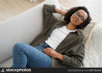 Relaxed serene young mixed race woman resting on comfortable sofa at home, calm relaxed biracial lady enjoy afternoon nap, breathing fresh air, lying on cozy couch with soft comfy pillow.. Relaxed serene young mixed race girl resting lying on comfortable sofa, enjoy afternoon nap at home