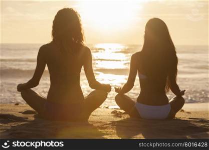 Relaxed sexy young brunette women or girls wearing bikini sitting on a deserted tropical beach at sunset or sunrise