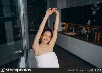 Relaxed smiling young woman use under eye anti-wrinkle patches on face, stretching herself in kitchen after shower. Happy girl enjoying morning beauty routine for healthy skin. Skincare treatment. . Pretty girl use under eye patches, stretching herself in kitchen after shower. Skincare treatment