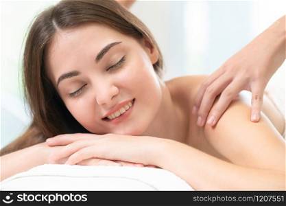 Relaxed woman getting shoulder massage in luxury spa with professional massage therapist in background. Wellness, healing and relaxation concept.. Woman gets back massage spa by massage therapist.