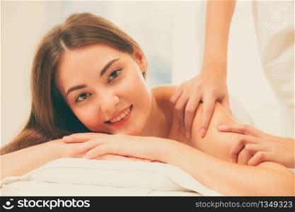 Relaxed woman getting shoulder massage in luxury spa with professional massage therapist in background. Wellness, healing and relaxation concept.