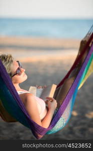 relaxed woman laying in hammock bed on beach and enjoy sunset while reading book