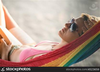 relaxed woman laying in hammock bed on beach and enjoy sunset while reading book