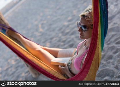 relaxed woman laying in hammock bed on beach and enjoy sunset while reading book