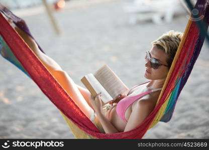 relaxed woman laying in hammock bed on beach and enjoy sunset while reading book