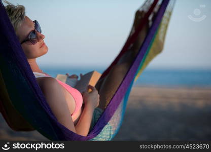 relaxed woman laying in hammock bed on beach and enjoy sunset while reading book