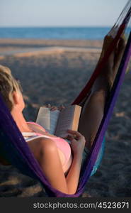 relaxed woman laying in hammock bed on beach and enjoy sunset while reading book