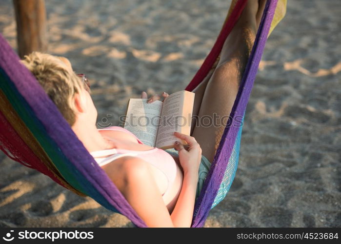 relaxed woman laying in hammock bed on beach and enjoy sunset while reading book