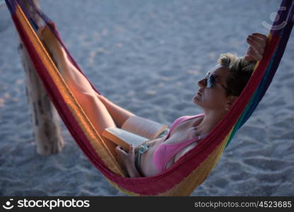 relaxed woman laying in hammock bed on beach and enjoy sunset while reading book