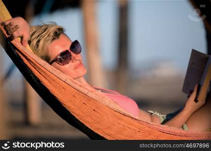 relaxed woman laying in hammock bed on beach and enjoy sunset while reading book