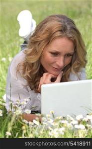 Relaxed woman lying in a field of daisies using her laptop