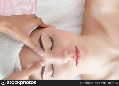 Relaxed woman lying on spa bed for facial and head massage spa treatment by massage therapist in a luxury spa resort. Wellness, stress relief and rejuvenation concept.