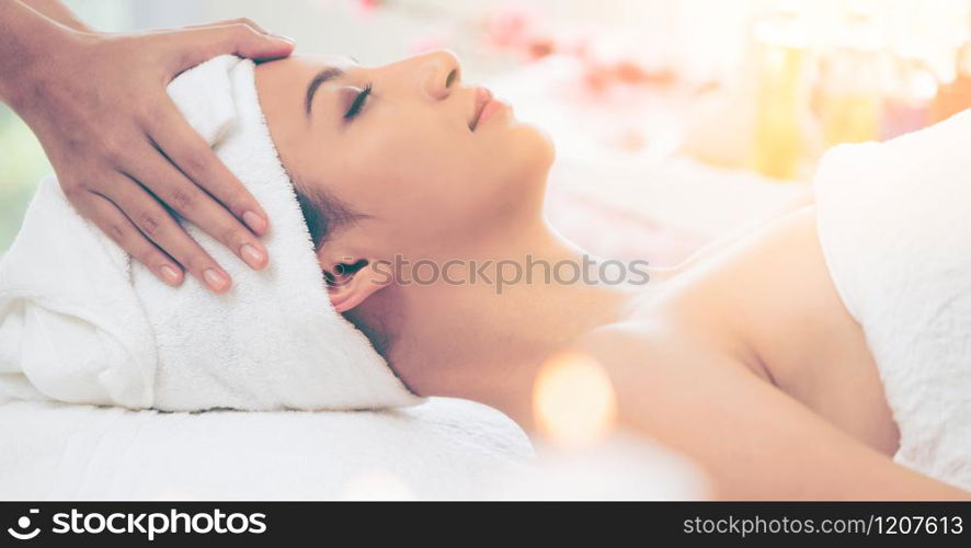 Relaxed woman lying on spa bed for facial and head massage spa treatment by massage therapist in a luxury spa resort. Wellness, stress relief and rejuvenation concept.